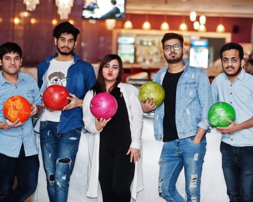Group of five south asian peoples having rest and fun at bowling club with balls at hands.